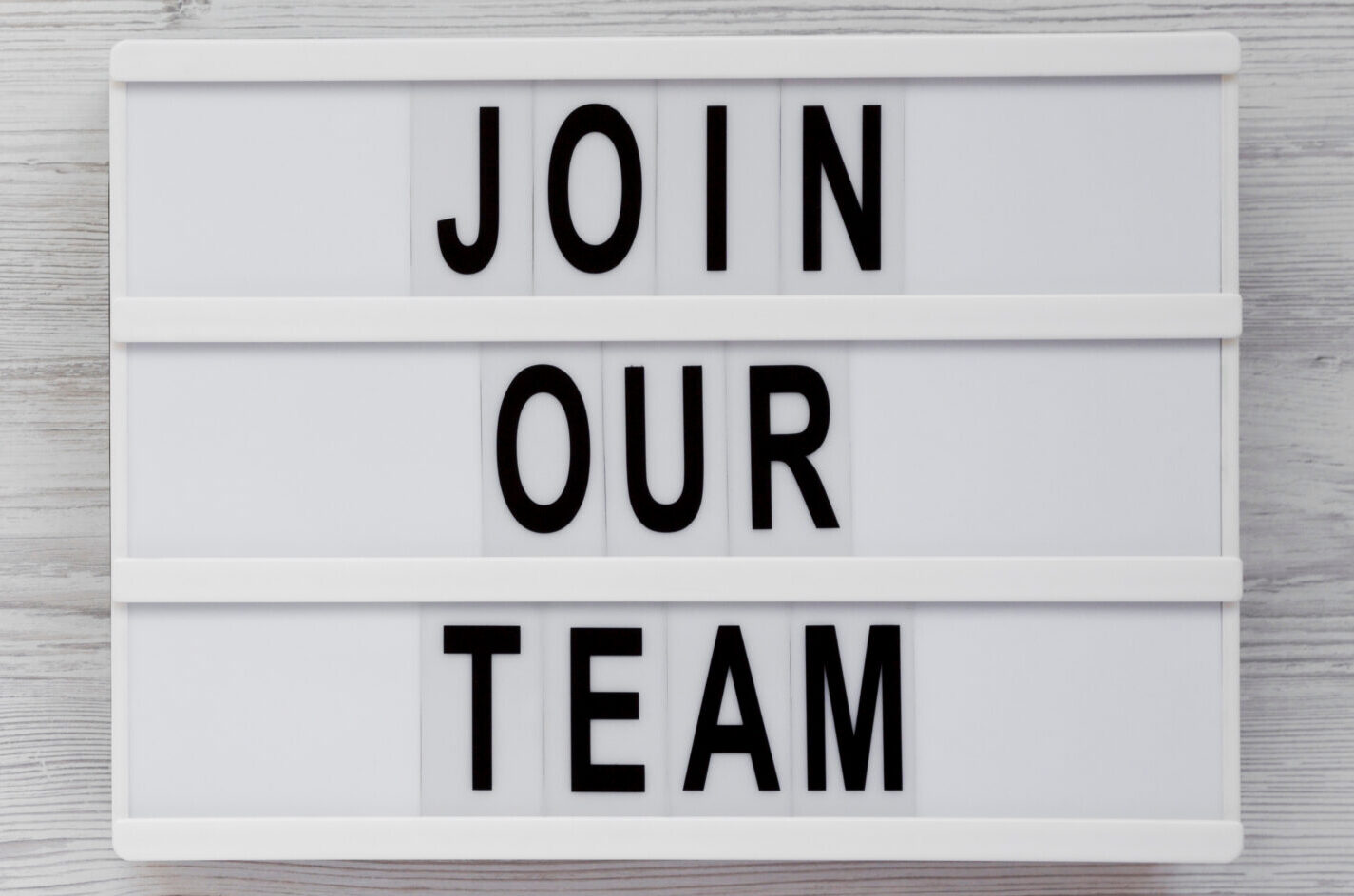 ‚Join our team‘ words on a lightbox on a white wooden background. Overhead, from above, flat lay. Space for text.